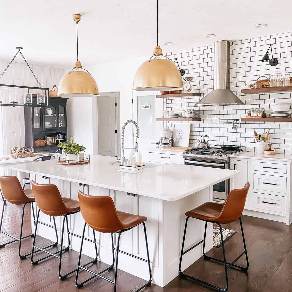 white kitchen with large brass pendants over island with subway tile up the wall