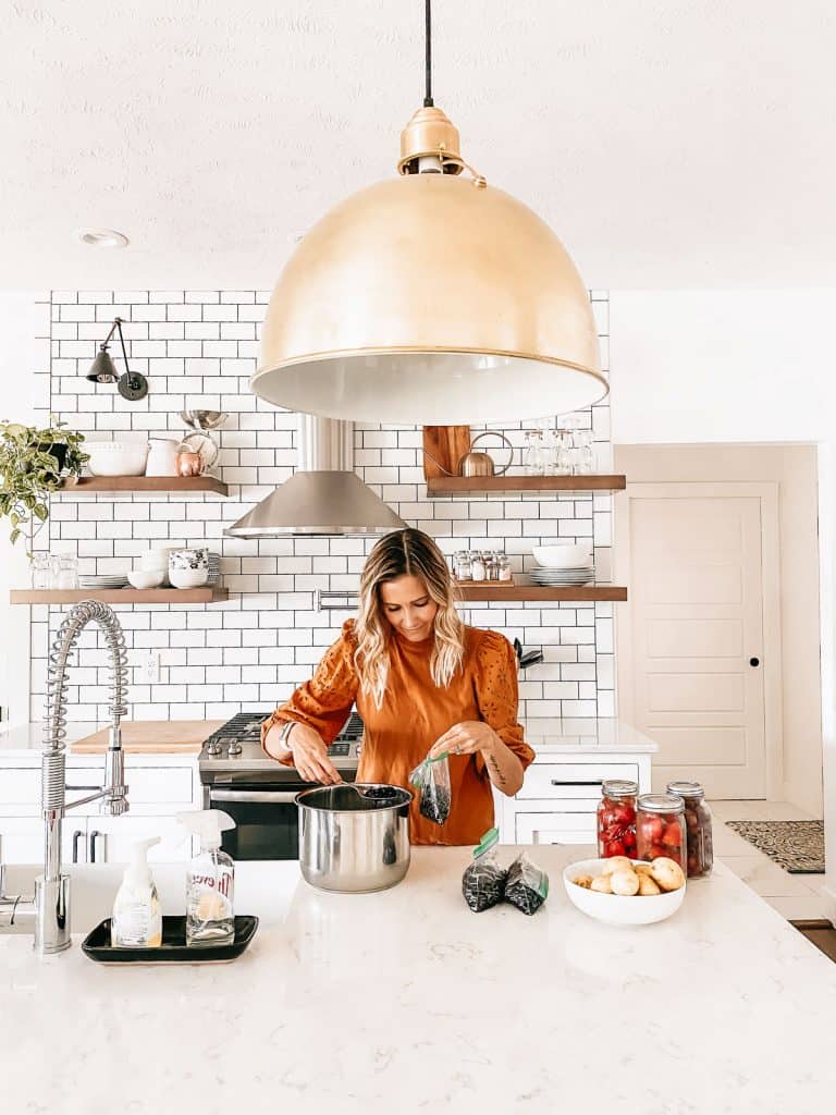 woman doing food storage in white kitchen with white subway tile and open shelving