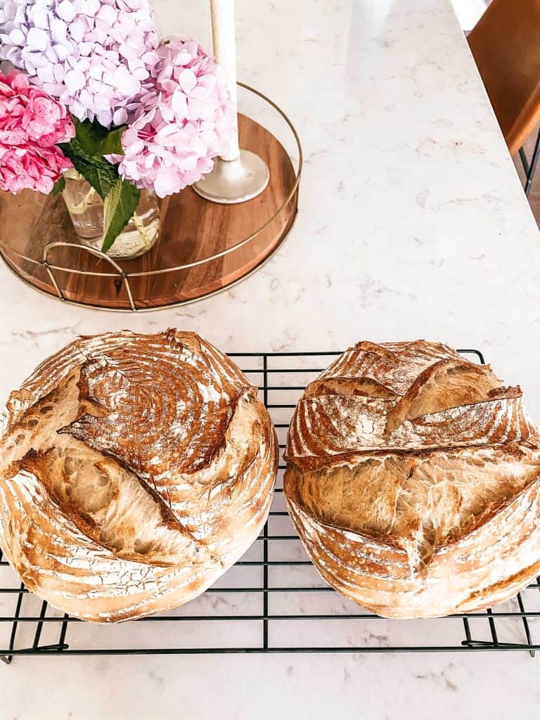 two loaves of homemade sourdough on a cooling rack on counter with hydrangeas in the background