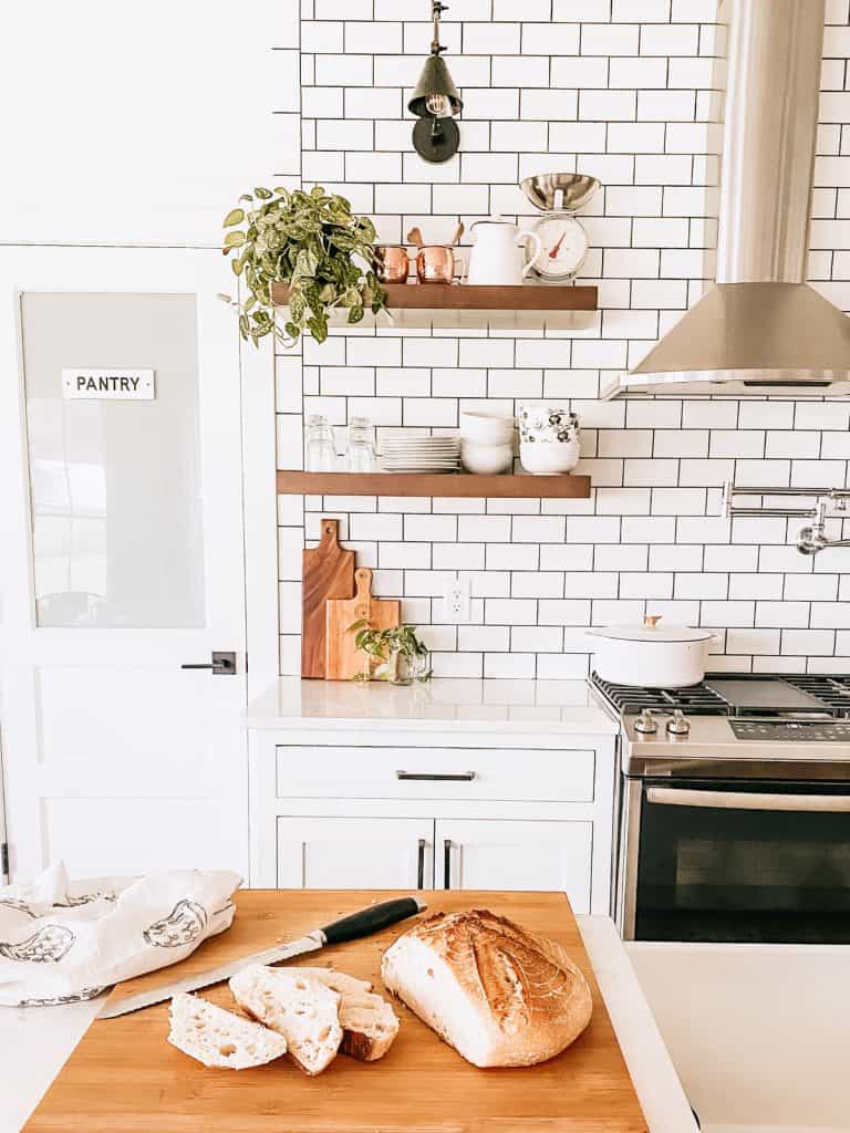 homemade sourdough bread on cutting board in white kitchen with open shelving and subway tile